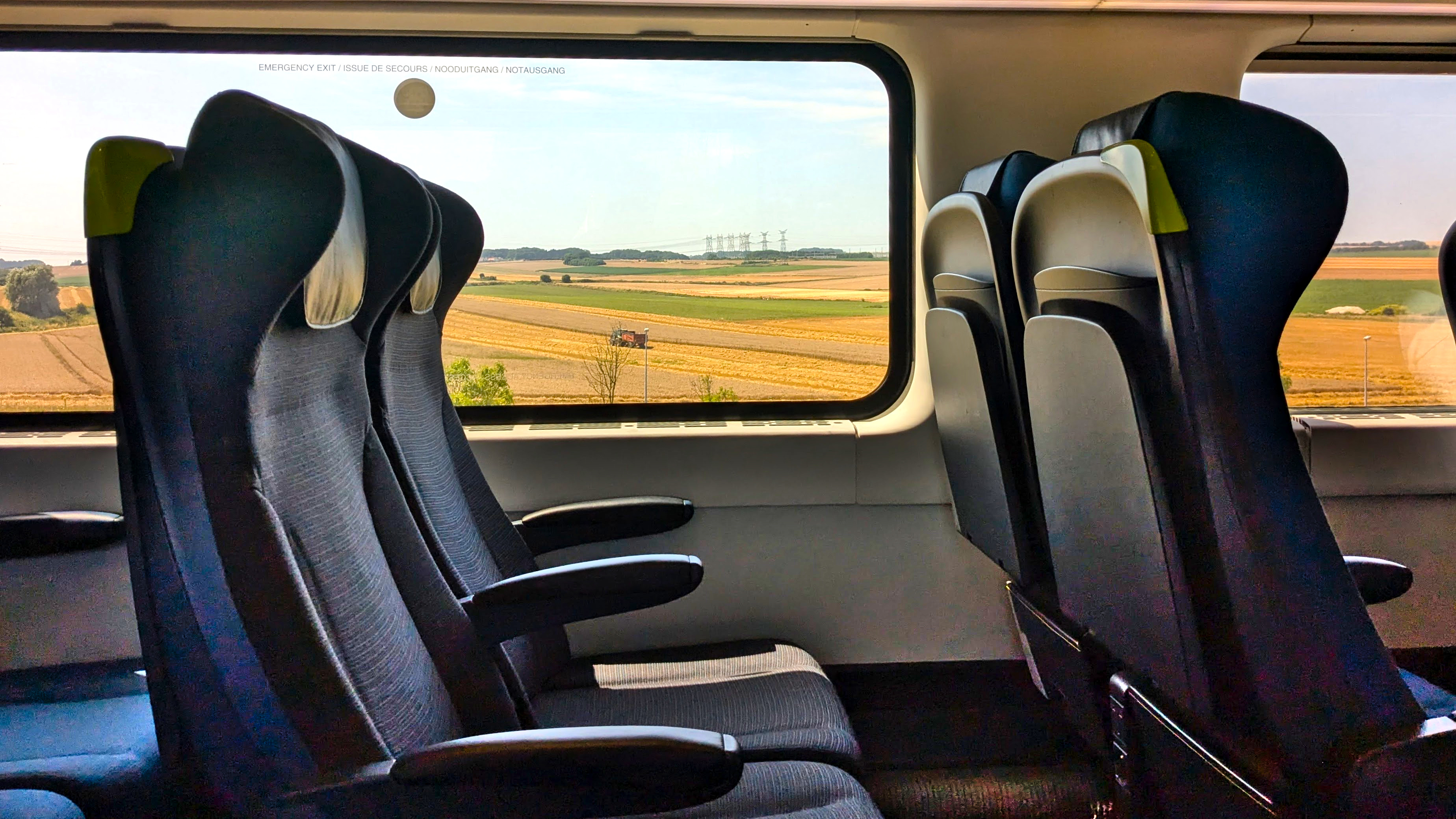 The interior of a train, looking out of a window past empty, past empty seats, you see rural landscape.